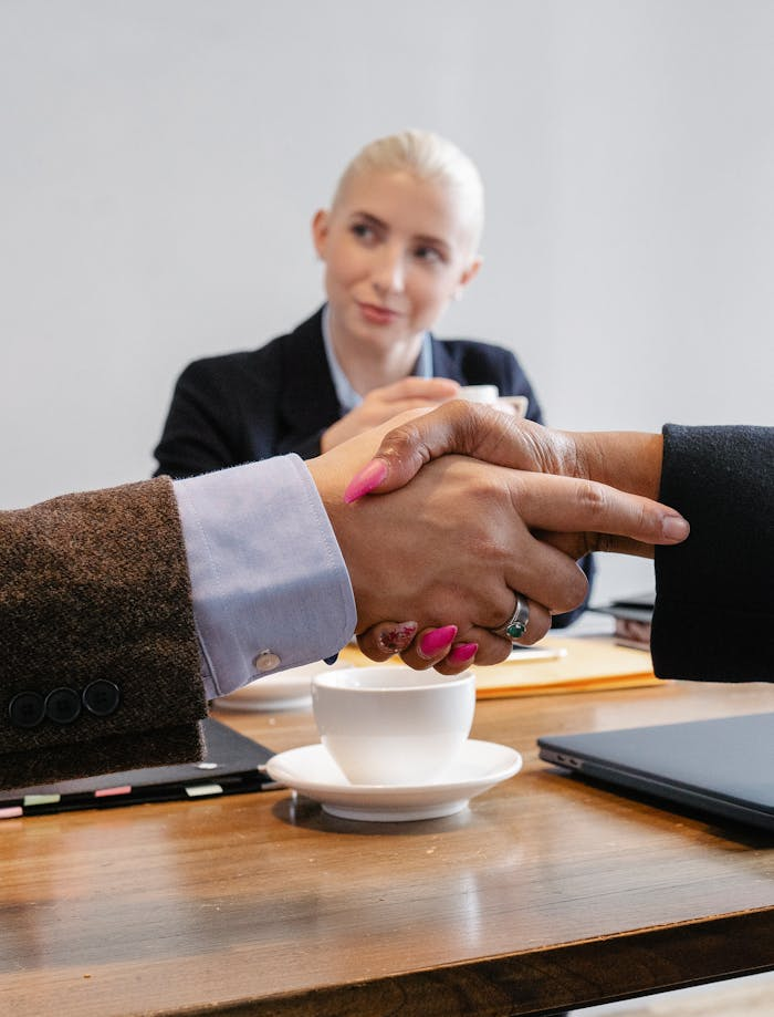 Contact Crop faceless multiracial coworkers sitting at table and shaking hands after successful agreement in workspace
