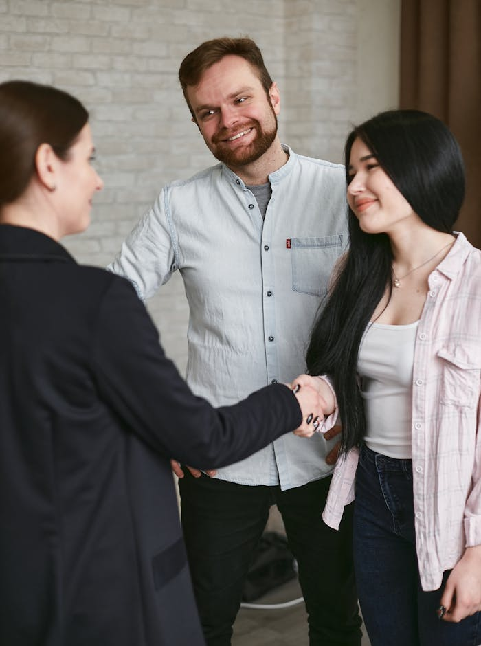 Services Three adults shaking hands in a professional meeting setting, showing agreement and positive interaction.