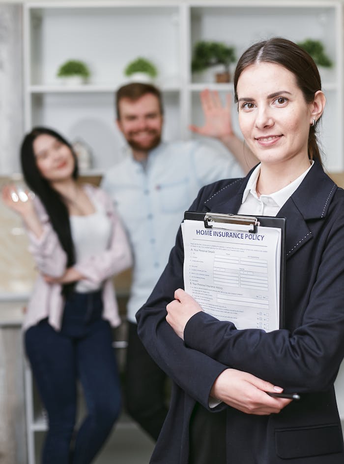 About A smiling businesswoman holding a home insurance policy with clients in the background.